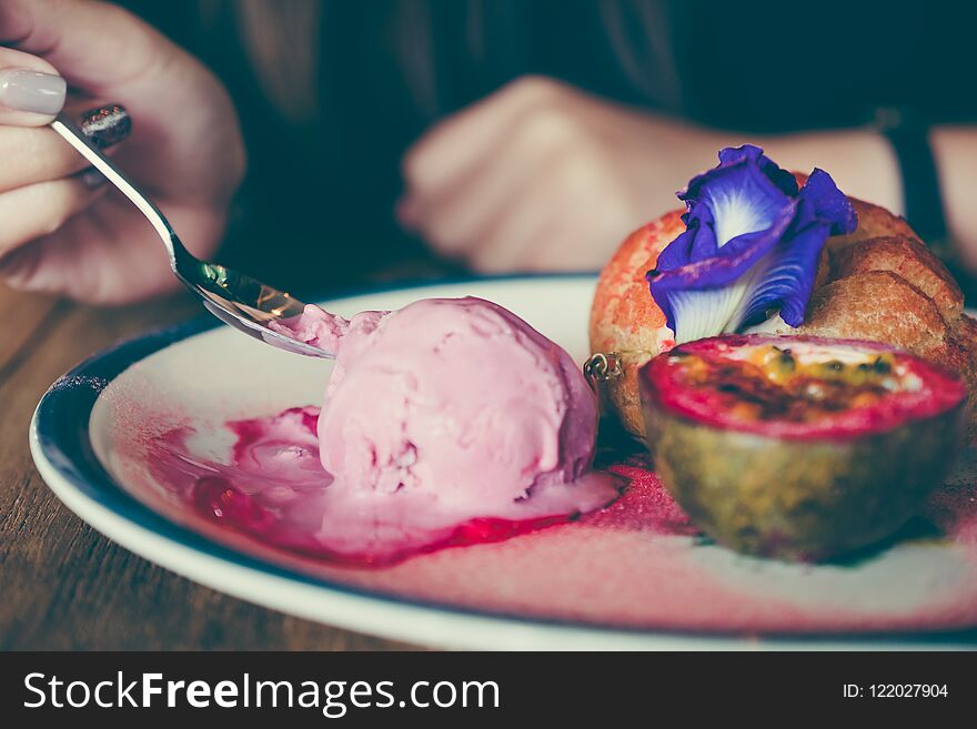 Closeup image of woman eating a dish of Choux cream , rose ice-cream and passion fruit with beautiful decoration