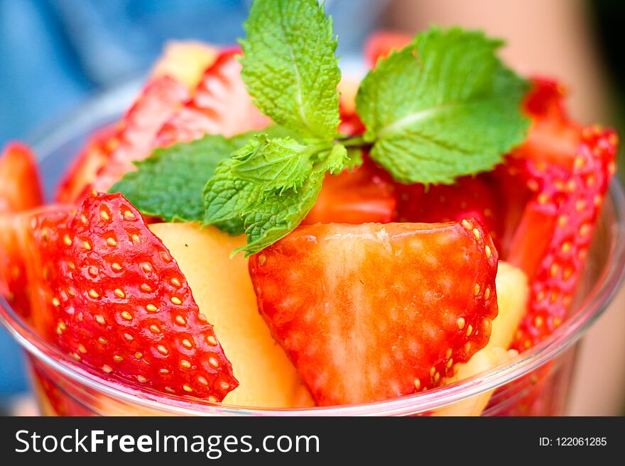 Fresh and fragrant sliced berries and fruits are stacked in a container. Yellow melon and red strawberry. Everything is decorated