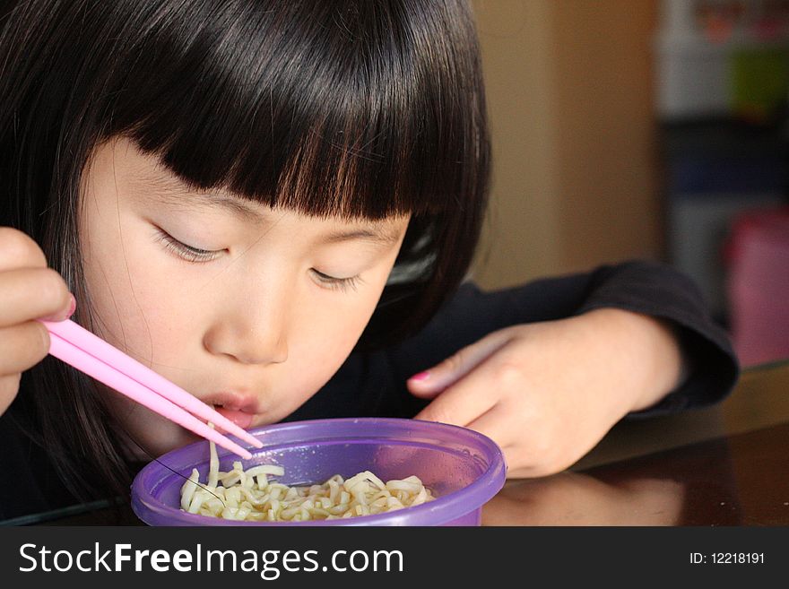 Asian Chinese Girl Eating Noodles with pink chop sticks from a purple bowl. Asian Chinese Girl Eating Noodles with pink chop sticks from a purple bowl
