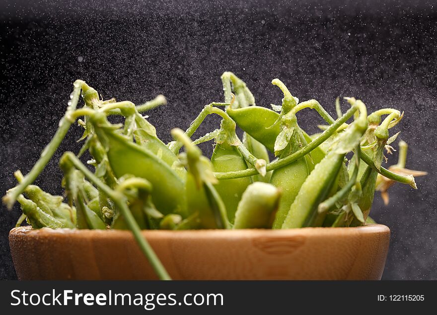 Photo of green pea pods in wooden cup on empty black background in studio