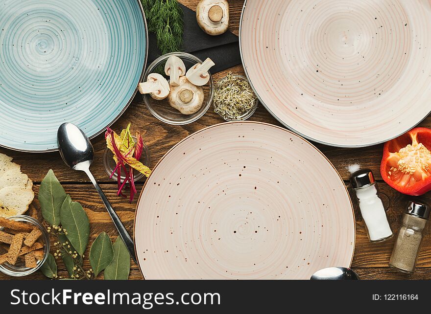 Set of three empty ceramic round plates on wooden table with food ingredients, mockup for meal, top view. Set of three empty ceramic round plates on wooden table with food ingredients, mockup for meal, top view