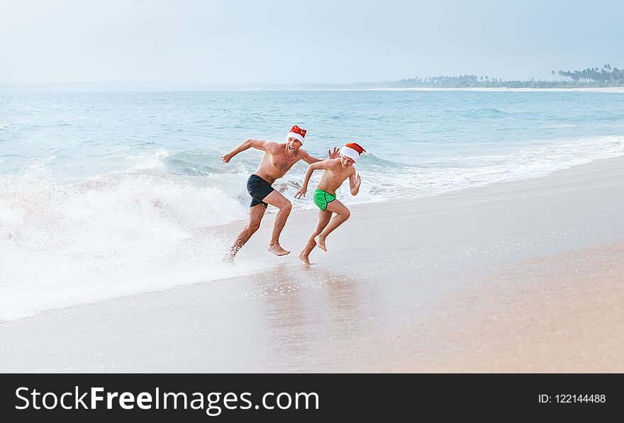 Father and son have a fun on ocean beach, run away from big waves. Christmas holiday time. Tropical vacation