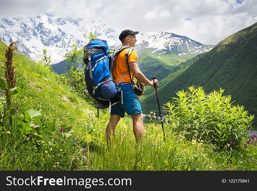 Tourist on a hike in the mountains on a bright sunny day. A young guy with a backpack in a mountainous area on a hiking trail.