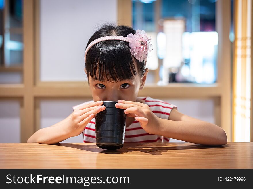 Asian little Chinese girl drinking hot green tea at a Japanese restaurant