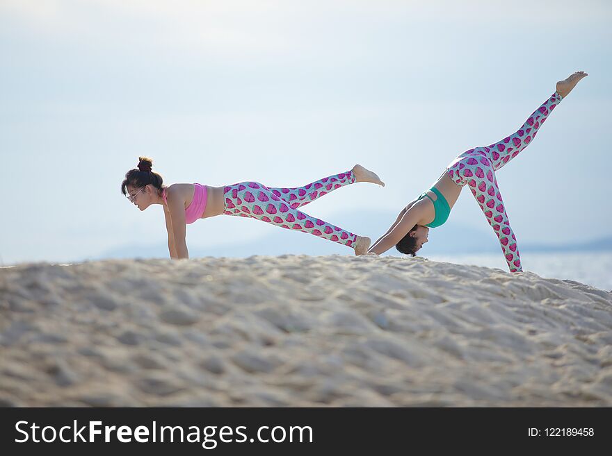 Two women playing yoga pose on sea beach