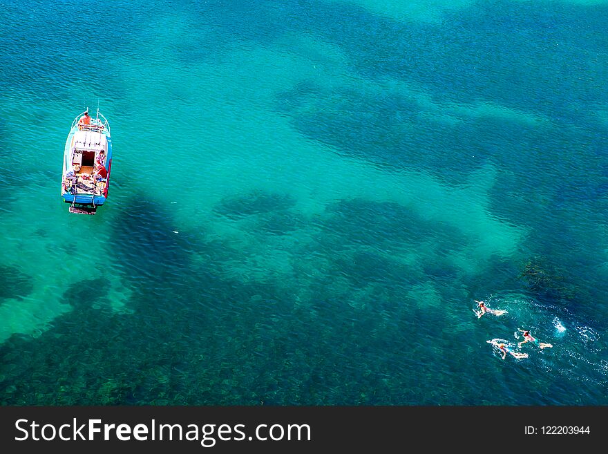 Aerial shot of turquoise water lagoon at hot summer day with white boat and people swimming around the boat.