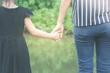 Woman And Cute Little Girl Holding Hands Together And Standing On Green Grass In The Public Park In Summer Time. Stock Photography