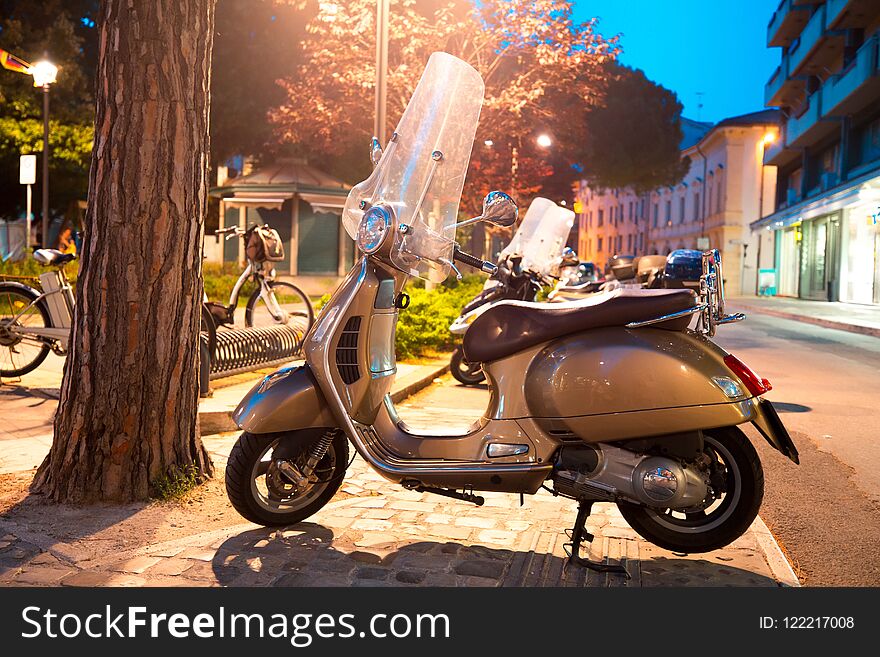 Scooter parked on the sidewalk in night city. Rimini, Italy. Theme of convenient transport.