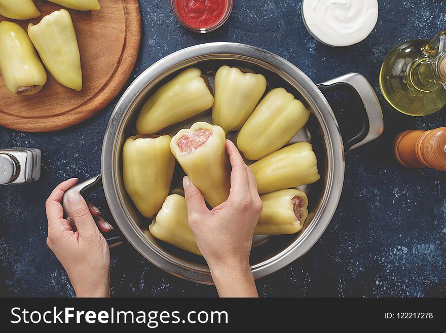 Hand puts raw stuffed pepper into the pan for cooking. Step by step recipe of homemade stewed stuffed sweet pepper top view.