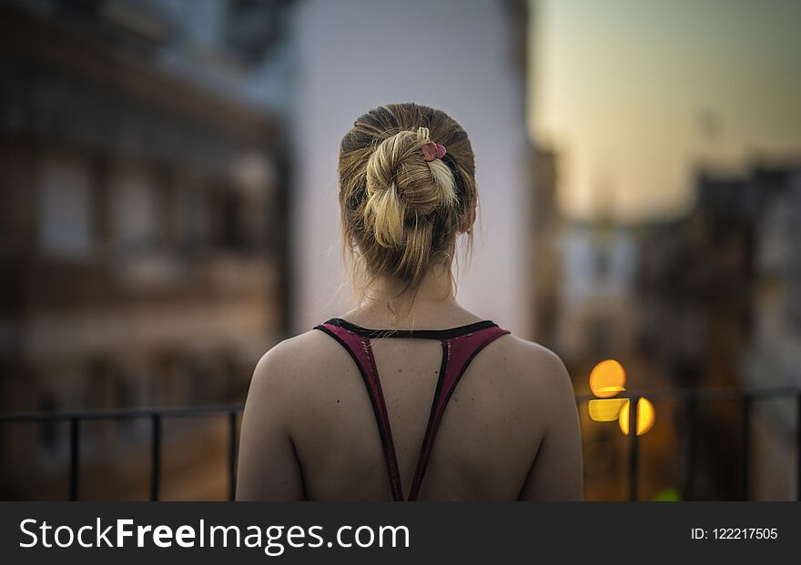 Back of a young woman looking at the cityscape from a terrace at sunset.