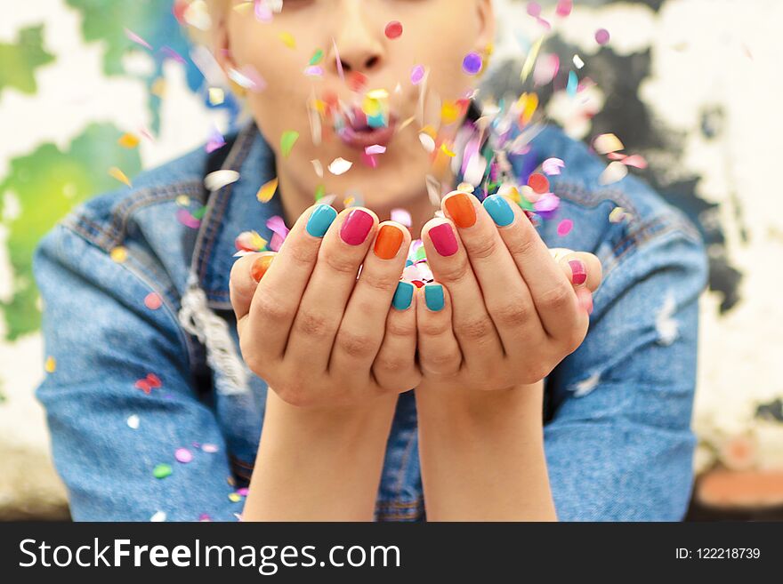 Fashionable girl with bright colorful nail designs blows confetti in her hands.Nails art.Color manicure.