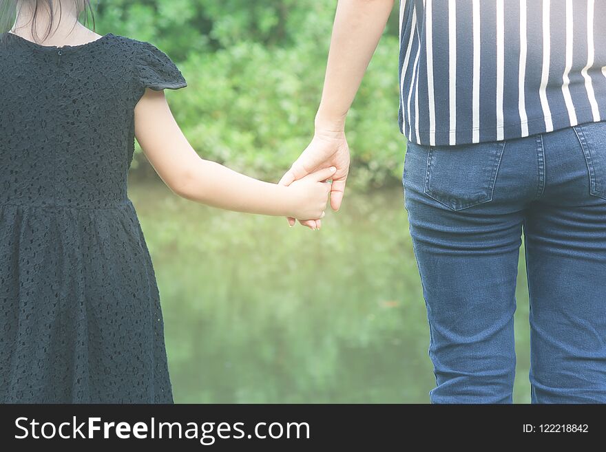 Woman and cute little girl holding hands together and standing on green grass in the public park in summer time.