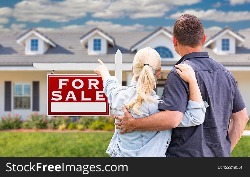 Young Adult Couple Facing and Pointing to Front of For Sale Sign