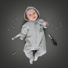 Baby In Grey Costume Lying On A Play Mat And Pretending He Is A Real Repairer Stock Photo