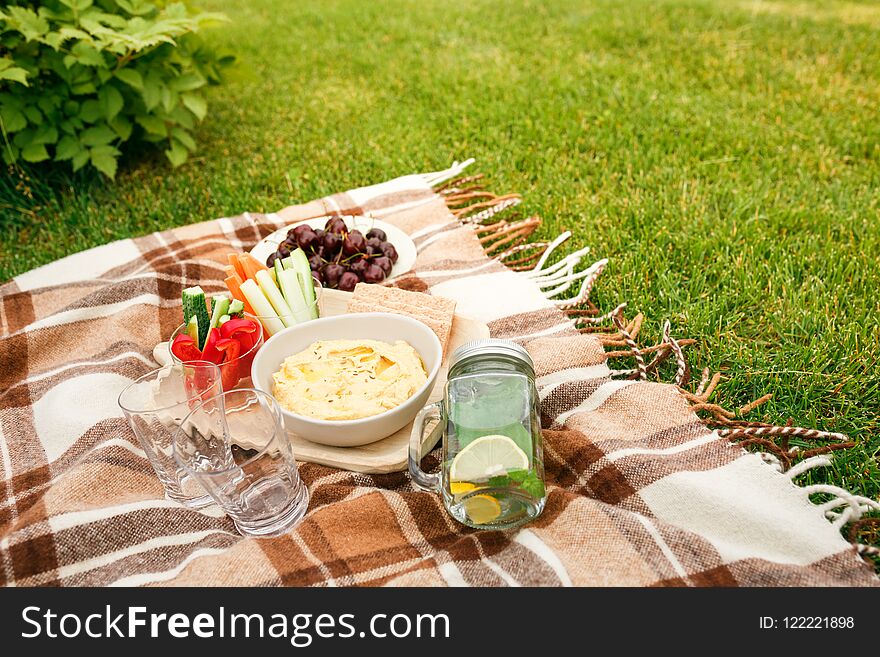 Picnic on the grass in the Park, on a checkered brown plaid snacks, vegetables, fruits, water in the Bank and glasses, without pe