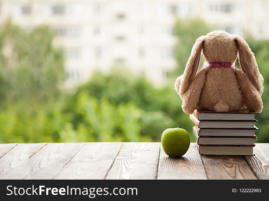 Toy Bunny sitting back, lie next to a stack of books and a green Apple. Concept in anticipation of the new school year.