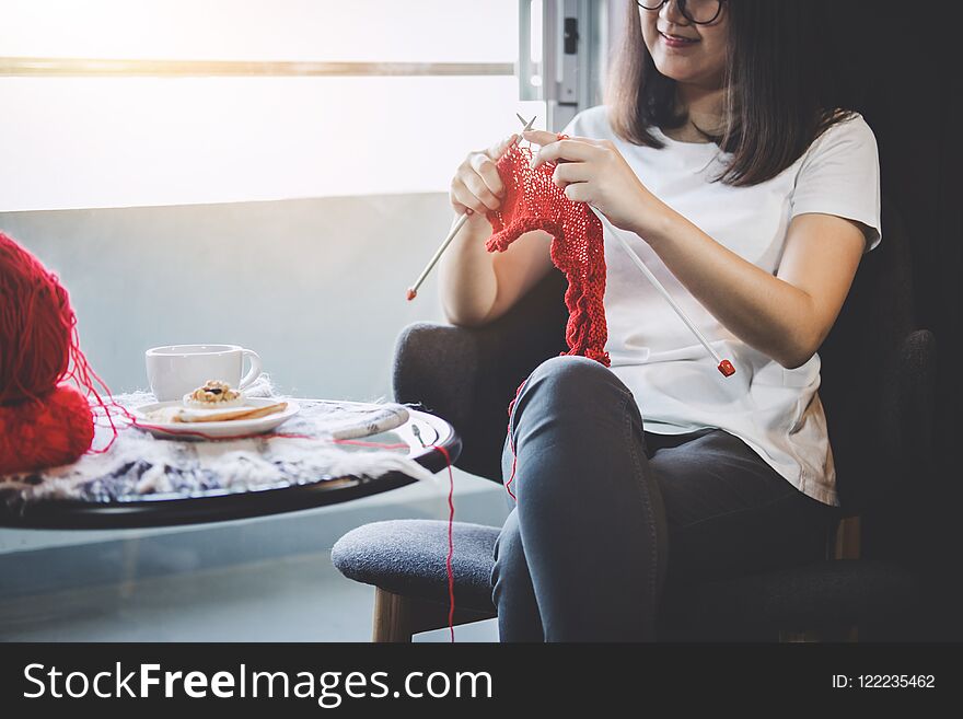 Close up shot of young woman hands knitting a red scarf handicraft in the living room on terrace at home