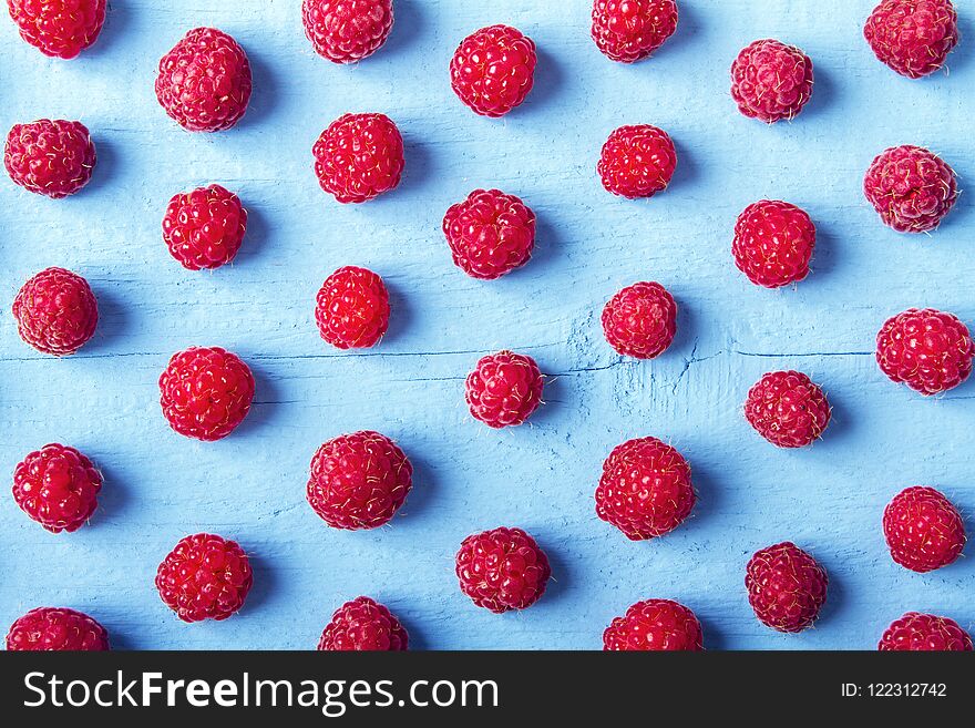 Many fresh raspberries on blue wooden background. Bright texture for design. Top view.