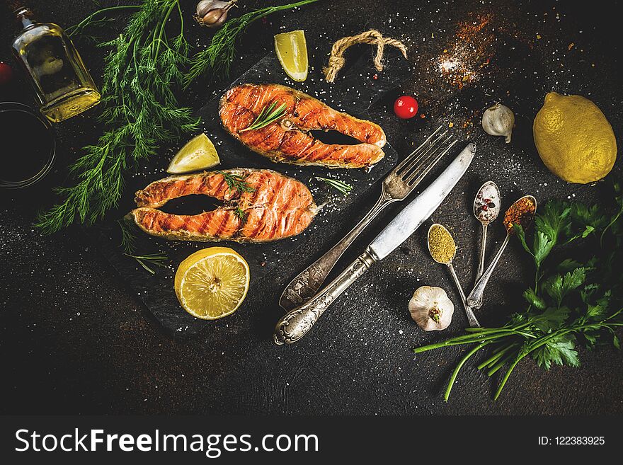 Grilled salmon fish steaks with ingredients lemon, herbs, olive oil, slate cutting board, dark rusty background copy space