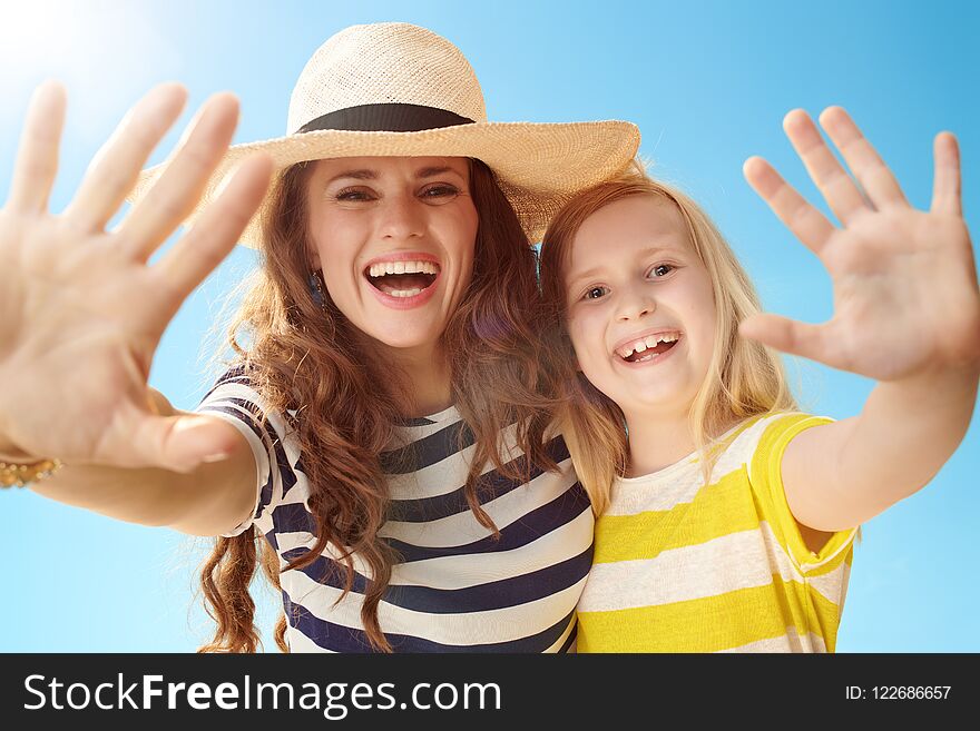 Happy young mother and daughter greeting against blue sky