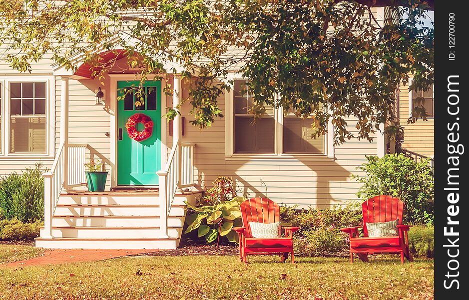 A small cozy wooden traditional American house with wooden chairs by the porch. Autumn sunny day. Vintage style.