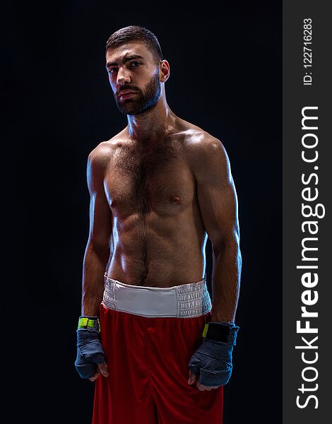 Boxing man ready to fight. Boxer with strong hands and clenched fists in blue straps against a black background