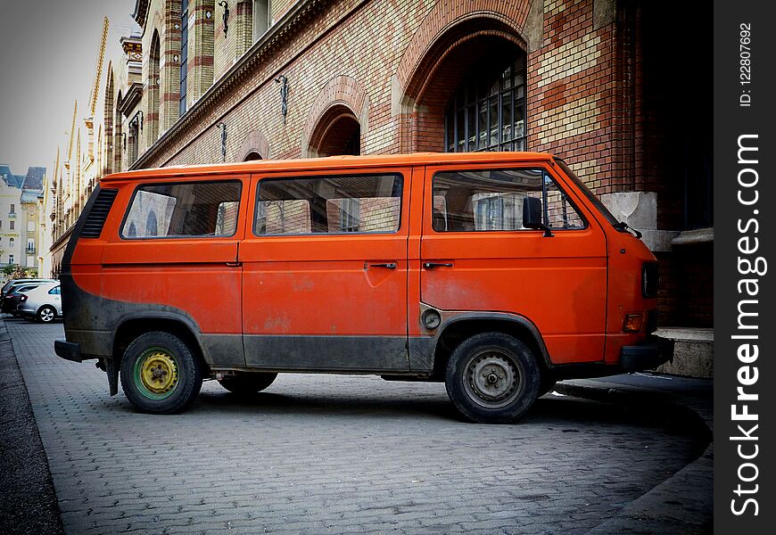 old European orange color camper mini van in urban setting in side view with classic building exterior background. old European orange color camper mini van in urban setting in side view with classic building exterior background