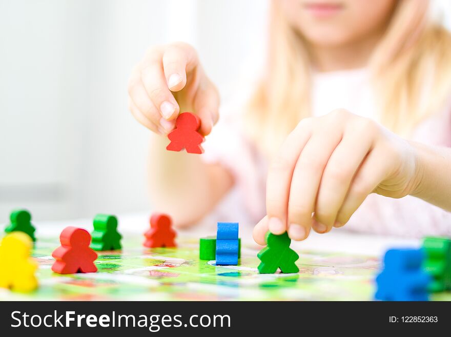 little blonde girl hold red people figure in hand. yellow, blue, green wood chips in children play - Board game and kids leisure c