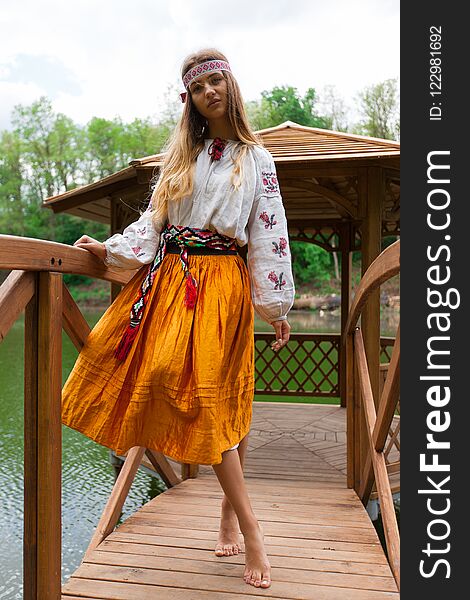 Beautiful slender Ukrainian in embroidery in windy weather enjoys a rest on the lake on a summer sunny day. Beautiful slender Ukrainian in embroidery in windy weather enjoys a rest on the lake on a summer sunny day