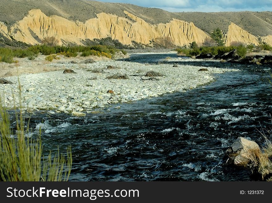 Clear water stream flows across shingle bank. Clear water stream flows across shingle bank