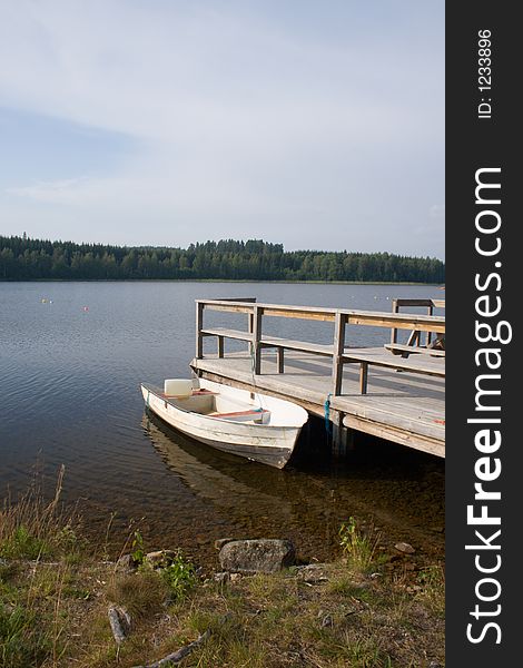 Small white boat moored to a wooden pier on a lake. Small white boat moored to a wooden pier on a lake