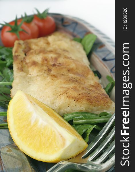 A close shot of a fish snack consisting of grilled and battered bream, rocket and cherry tomato salad with a larger slice of lemon. Shallow depth of field. A close shot of a fish snack consisting of grilled and battered bream, rocket and cherry tomato salad with a larger slice of lemon. Shallow depth of field.