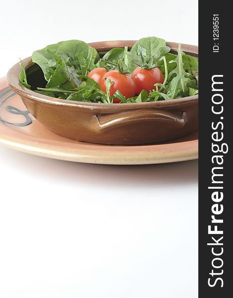 A mixed green salad and cherry tomatoes in a stoneware casserole sitting on a stoneware platter. A mixed green salad and cherry tomatoes in a stoneware casserole sitting on a stoneware platter.