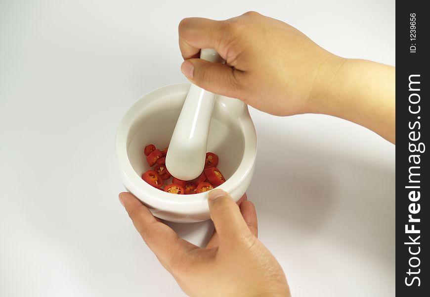 Grinding red chillies in a white mortar and pestle. Grinding red chillies in a white mortar and pestle