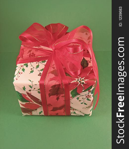 Christmas present wrapped in poinsettia pattern paper and a red bow; green background. Christmas present wrapped in poinsettia pattern paper and a red bow; green background.