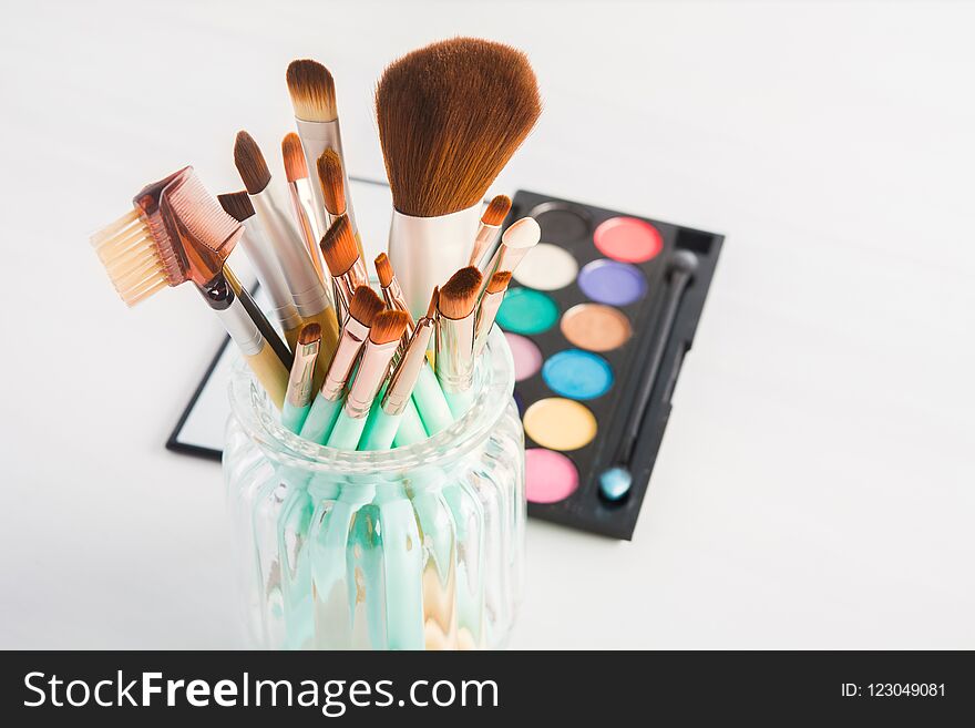 Different makeup brushes in jar on light background, selective focus