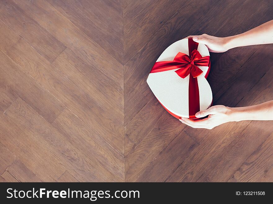 Human hands holding a present gift with red ribbon in wooden background - from top view - with copy space.