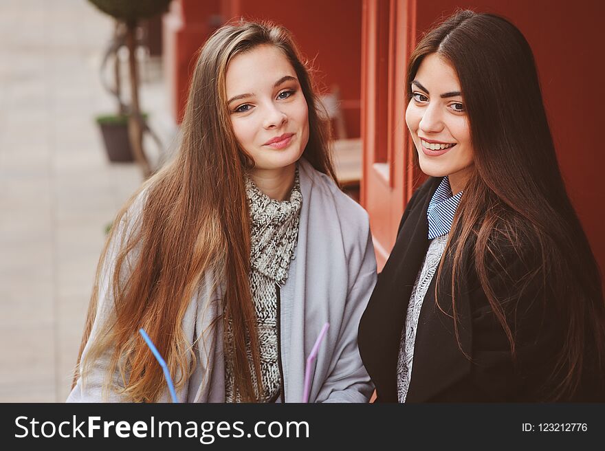 Two happy girl friends talking and drinking coffee in autumn city in cafe. Meeting of good friends, young fashionable students with natural make up.