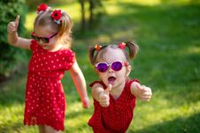 Two Cute Little Girlfriends Having Fun In The Yard. Little Girl Show Sight Thumbs Up And Good Luck. Dressed In Bright Red Dresses Stock Photo