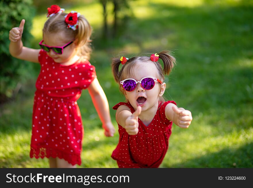 Two cute little girlfriends having fun in the yard. little girl show sight thumbs up and good luck. dressed in bright red dresses