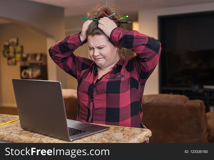 Young female college student sitting in front go laptop computer hands on head pencils in hair stressed look on her face. Young female college student sitting in front go laptop computer hands on head pencils in hair stressed look on her face