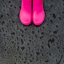 Trendy Bright Pink Rubber Boots On Black Wet Surface Covered With Raindrops. Stock Photography