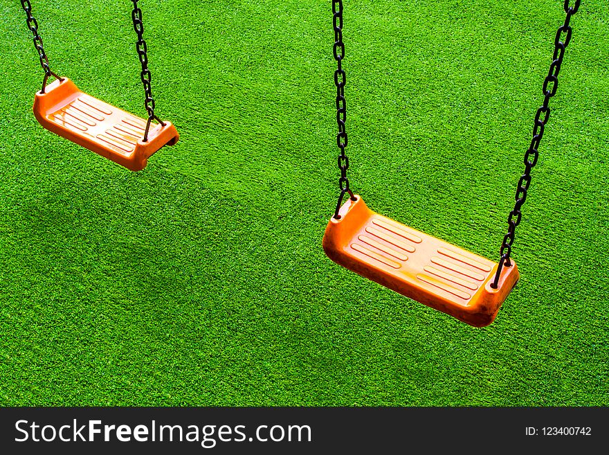 Double vivid orange color Swing seat on the artificial grass school yard. Double vivid orange color Swing seat on the artificial grass school yard