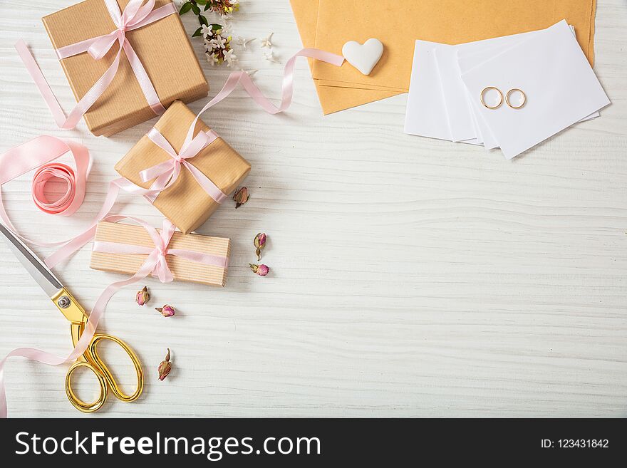 Wedding preparation. Flat lay and top view of presents and wedding invitations on a white wooden tabletop, copy space.