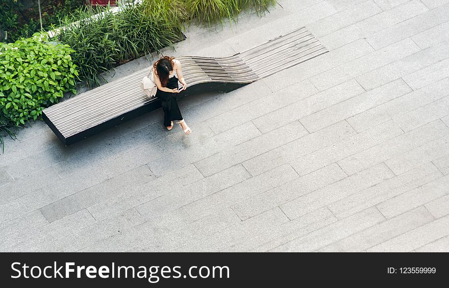 top aerial view woman uses smartphone sit on wooden bench at walkway pedestrian, concept of social still life.
