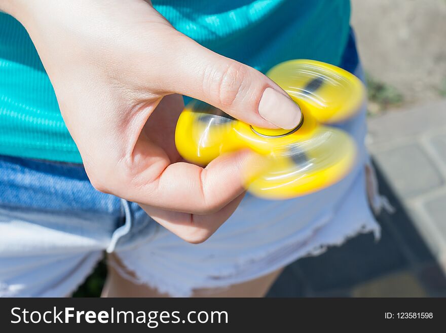 Close up photo of rotating yellow fidget spinner in girl`s hands cropped closeup view photo of teen teenager playing with spinner