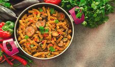 Mediterranean Eggplant Pasta In Pot With Tomatoes, Red Pepper And Parsley On Grey Background. Stock Photo
