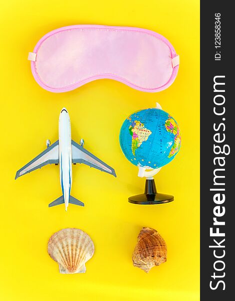 Flat Lay with plane, sleeping eye mask, shell and globe on yellow colourful trendy modern fashion background. Vacation travel summer weekend sea adventure trip concept. Flat Lay with plane, sleeping eye mask, shell and globe on yellow colourful trendy modern fashion background. Vacation travel summer weekend sea adventure trip concept