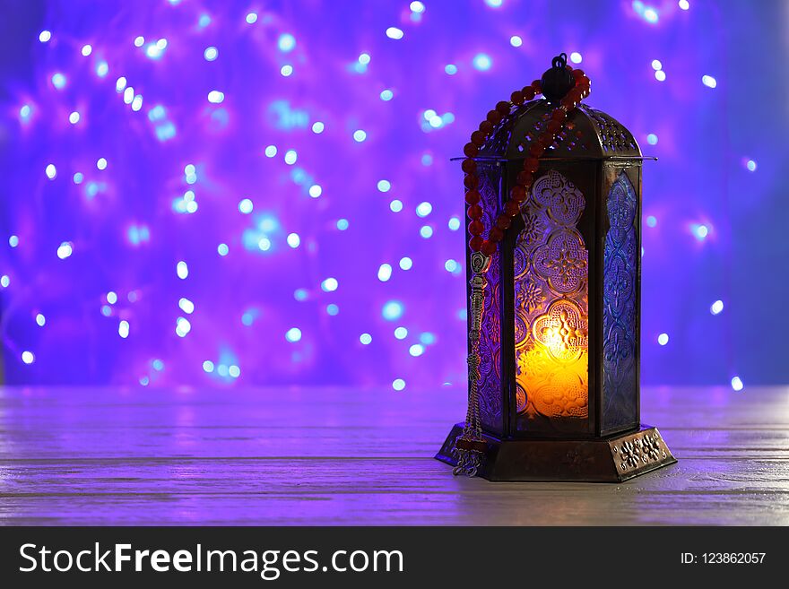 Muslim lamp with candle on table against blurred fairy lights. Fanous as Ramadan symbol