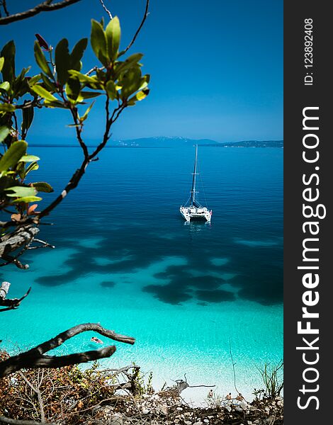 White catamaran yacht at anchor on clear azure surface with dark pattern in calm blue lagoon. Unrecognizable tourists relax on airbed in water near the beach.